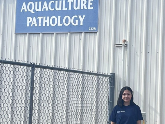 Dr. Magdalena Lenny Situmorang in front of a sign saying "Aquaculture Pathology"