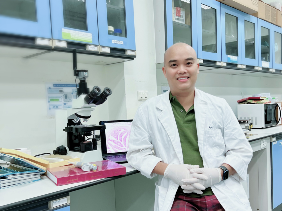 Image of Henry Nguyen Dinh Hung in lab coat in front of a microscope