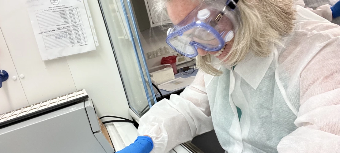 Image of a person in lab coat and goggles working inside of a fume hood